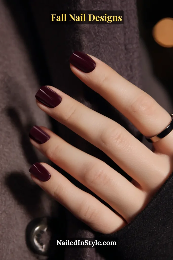 Hand with short velvet oxblood burgundy nails against a wool coat.
