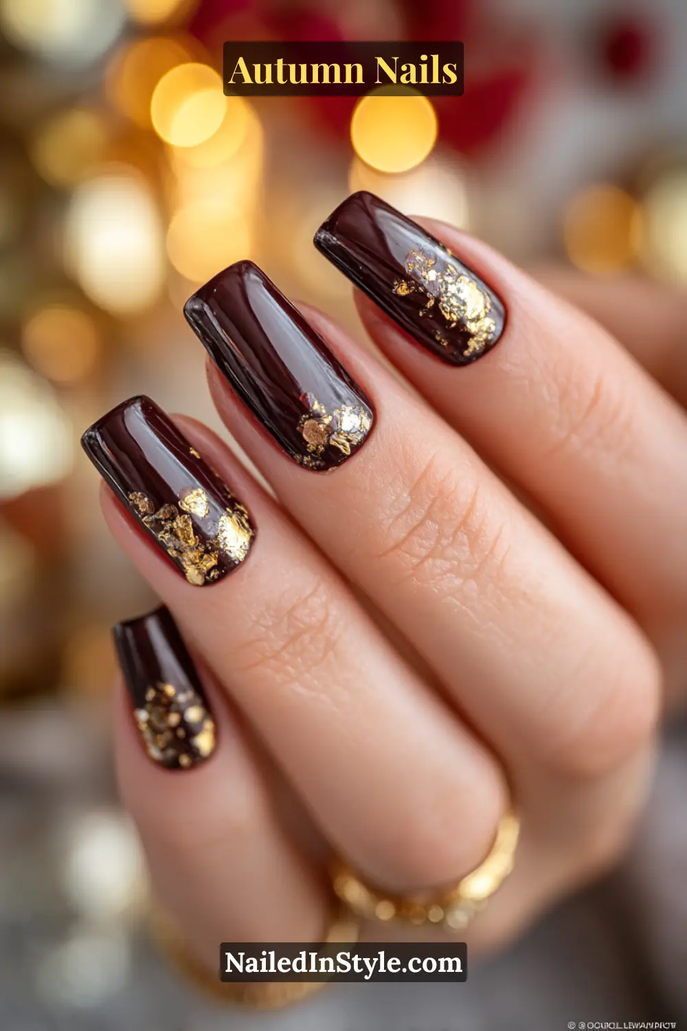 Close-up of burnished gold foil autumn nails with chocolate brown polish and metallic gold leaf flecks, glowing under party lights.