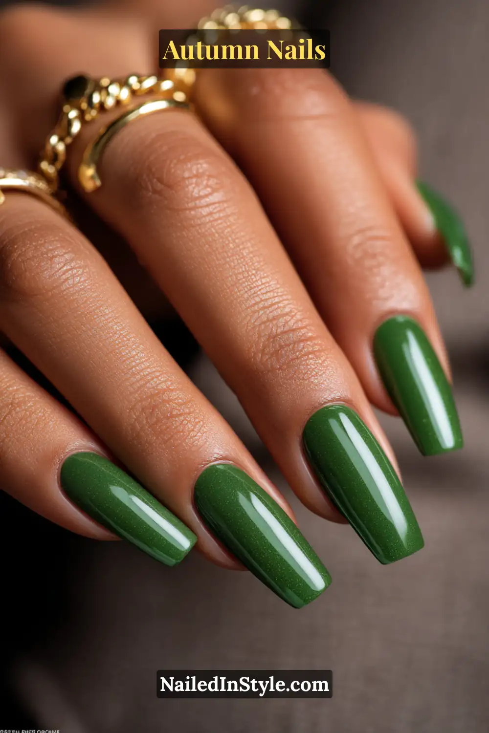 Close-up of emerald jewel gloss autumn nails with glossy emerald green cream polish, styled with chunky gold rings.