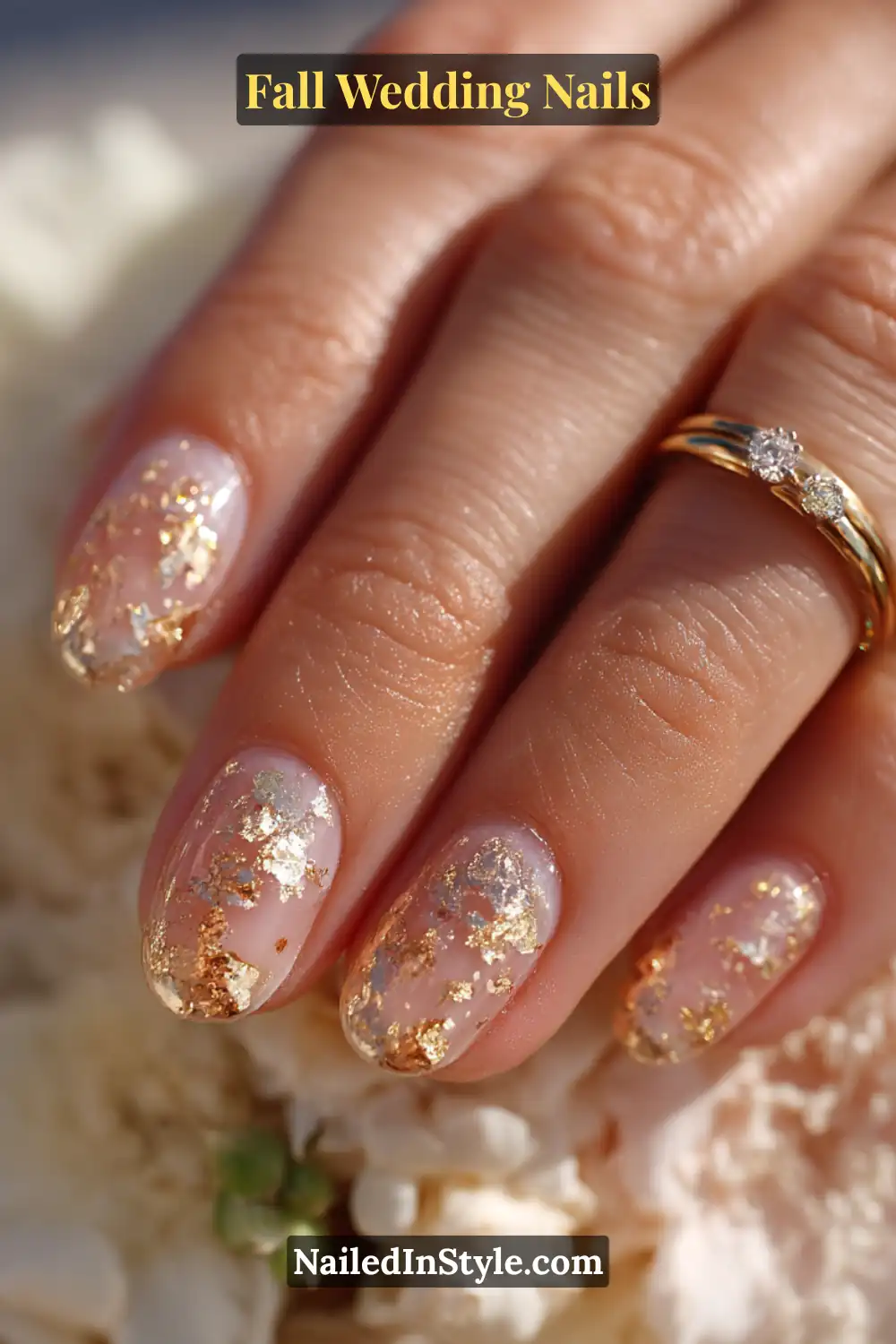 Close-up of bride’s hand with neutral base nails and scattered gold foil accents, paired with wedding rings.