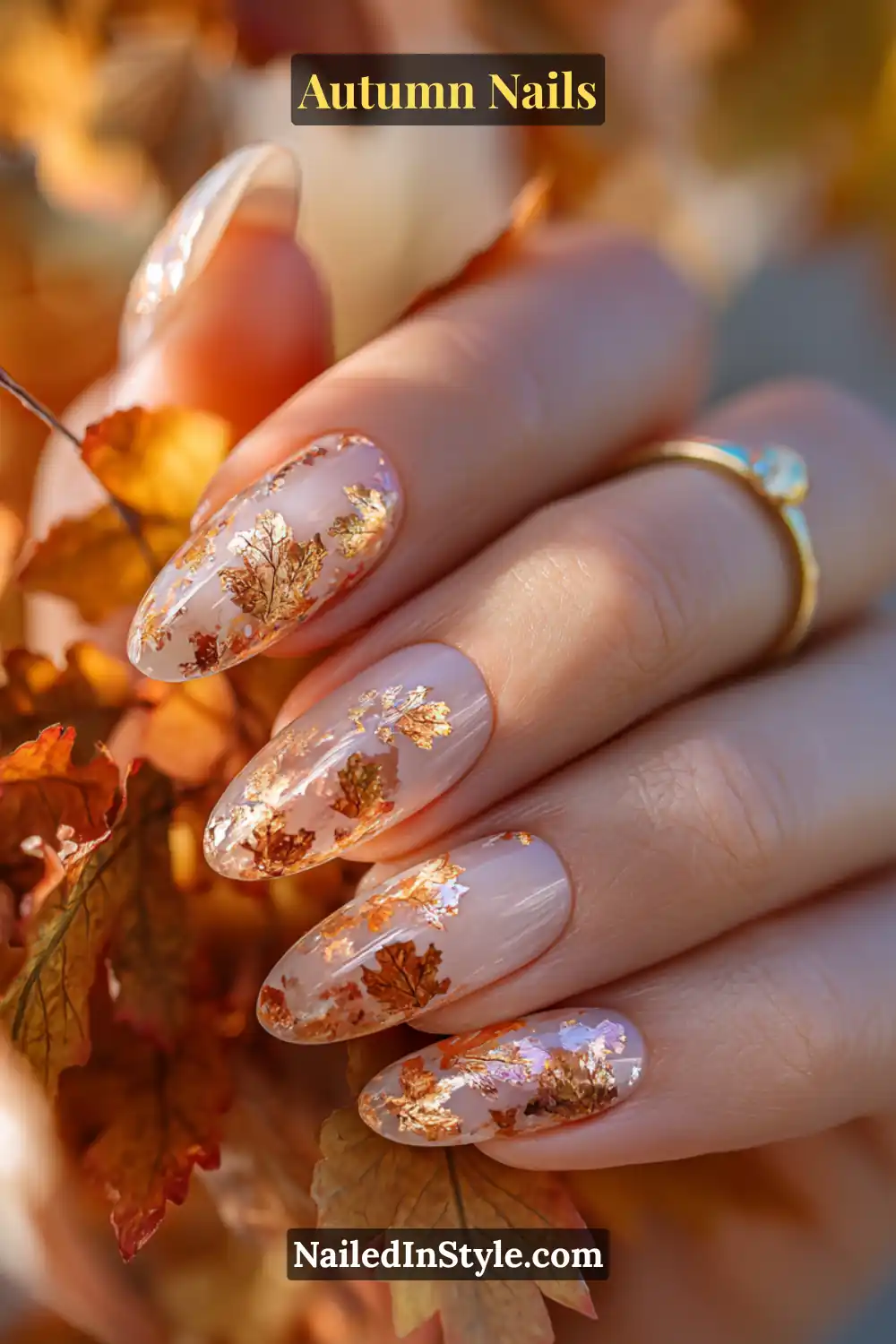 Close-up of maple leaf foil accents autumn nails with delicate foil leaf shapes in amber and copper, styled with real fall leaves.