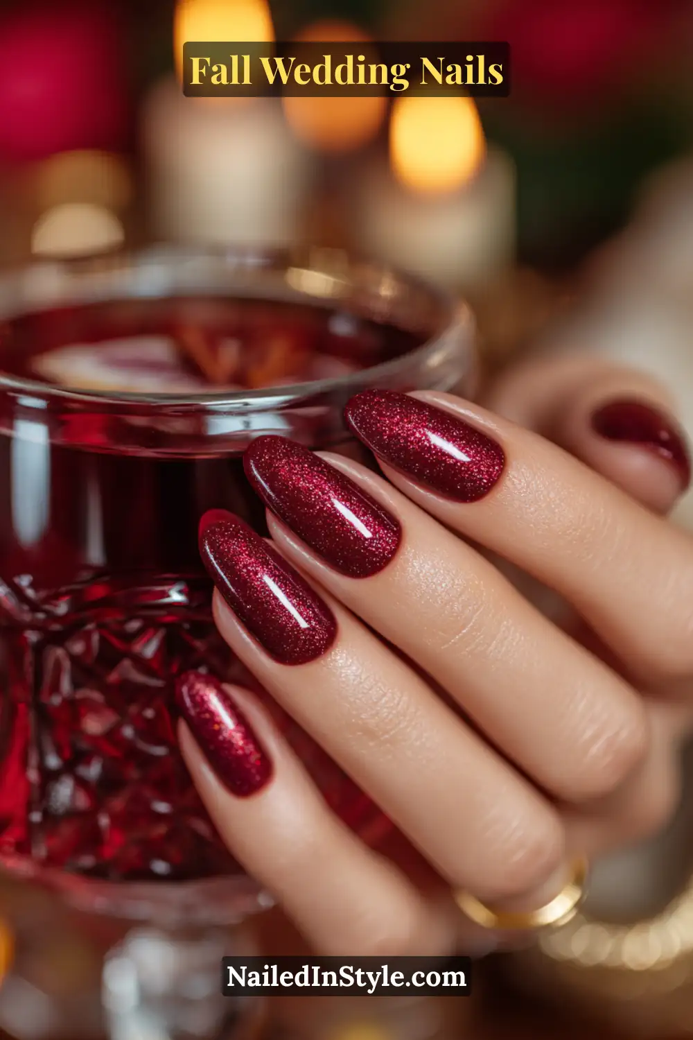 Bride’s hand with burgundy cat-eye shimmer nails holding a mulled wine glass.