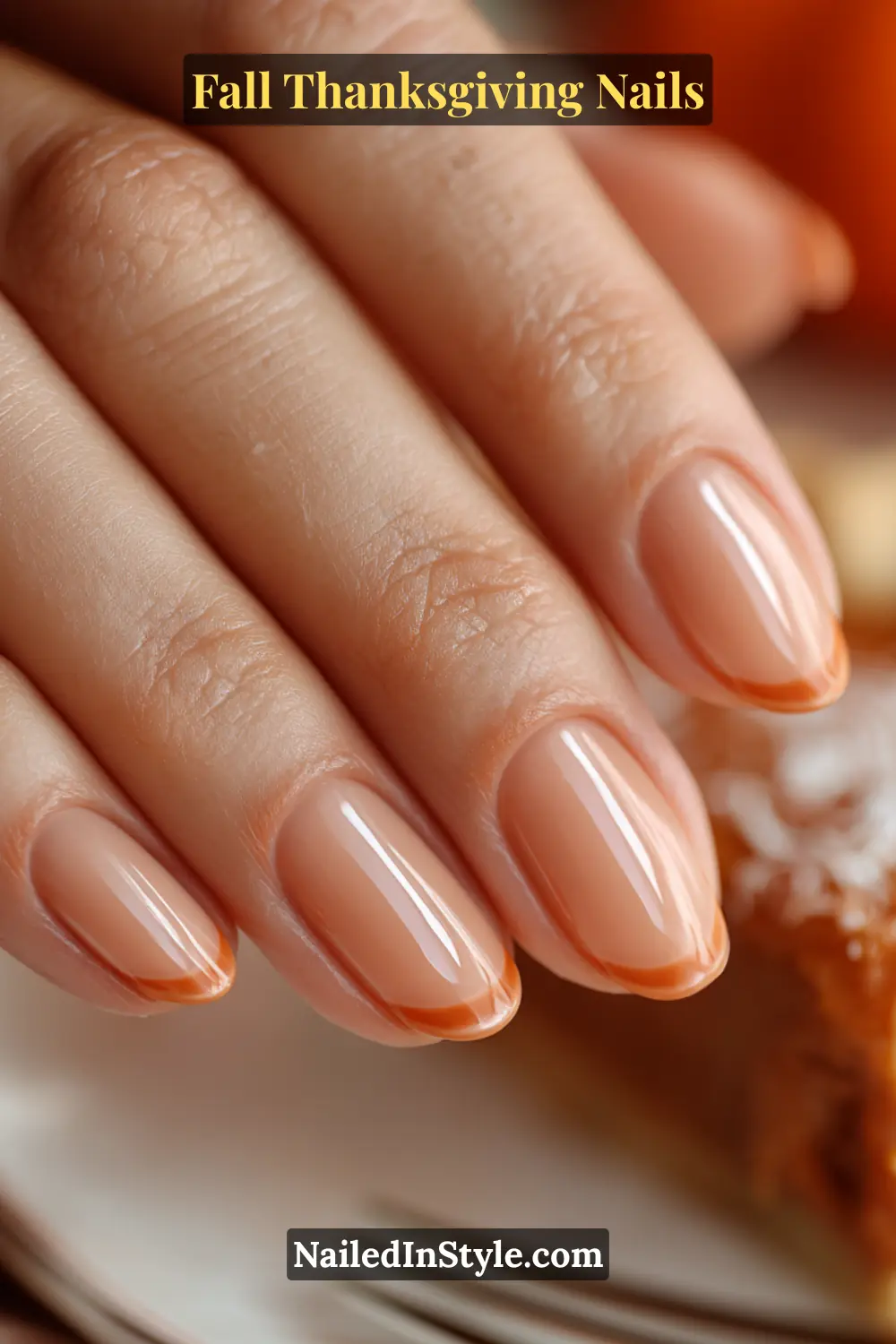 Fall Thanksgiving Nails Close-up of pumpkin spice micro-French Thanksgiving nails with sheer nude base and tiny pumpkin-orange French tips, styled with pumpkin pie.