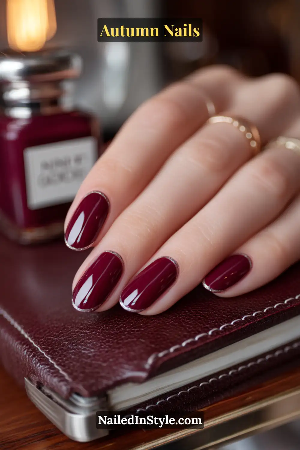 Close-up of spiced plum half-moon autumn nails with deep plum polish and bare half-moon detail, resting on leather-bound planner.
