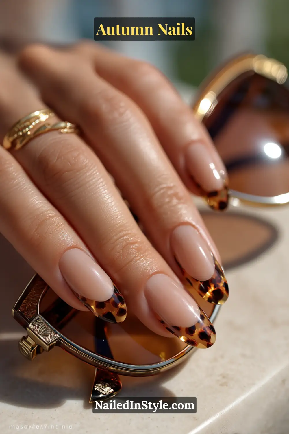 Close-up of tortoiseshell tips autumn nails with neutral base and caramel-black patterned French tips, styled with sunglasses.