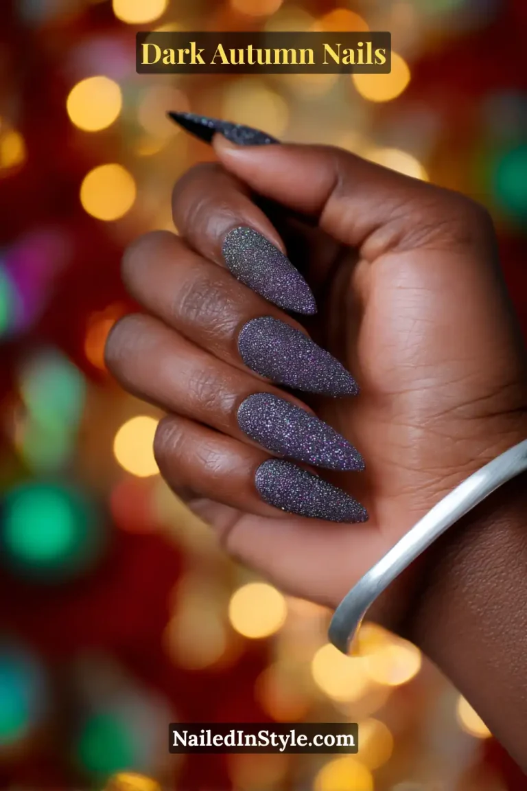Dark autumn nails in charcoal jelly with superfine glitter, styled on long stiletto nails against a twinkle light bokeh background.