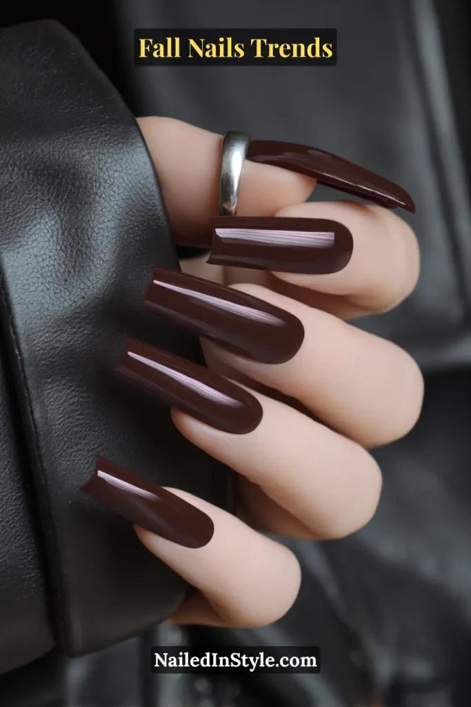 Fall deep mocha coffin nails in a glossy brown shade, styled with a leather jacket sleeve for a dramatic seasonal statement.