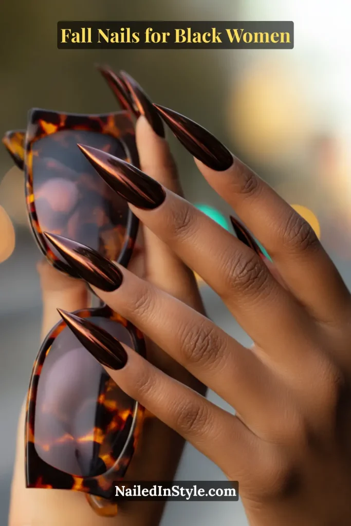 Fall nails for Black women featuring chestnut chrome stiletto nails in a rich metallic brown shade, styled with tortoiseshell sunglasses.
