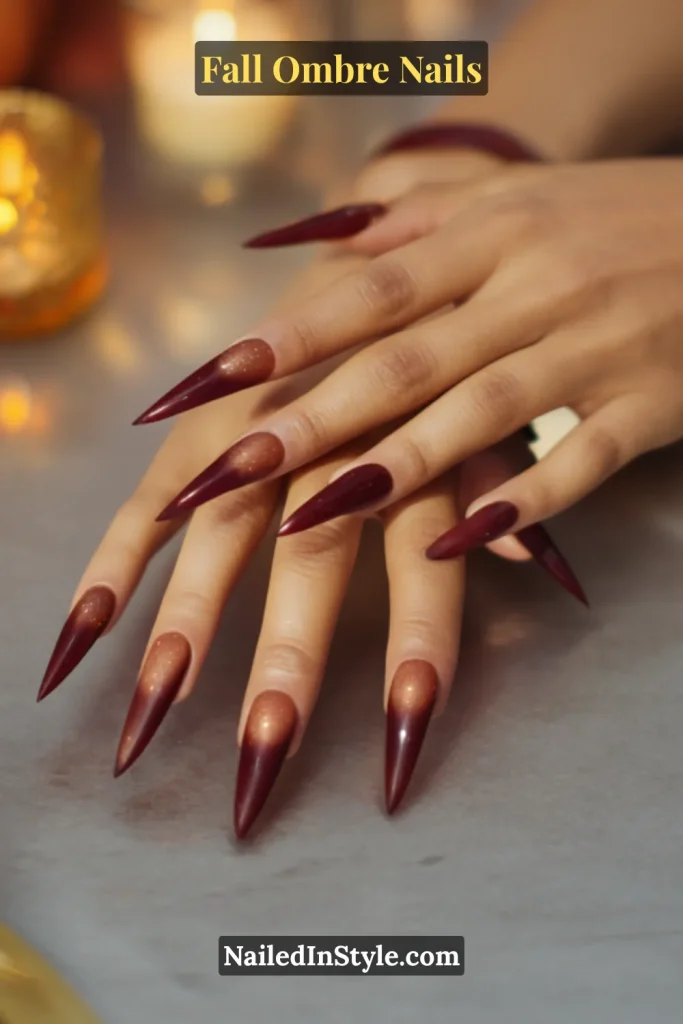 Fall ombre nails with warm copper blending into rich cranberry, styled on long stiletto nails by a candlelit dinner table.