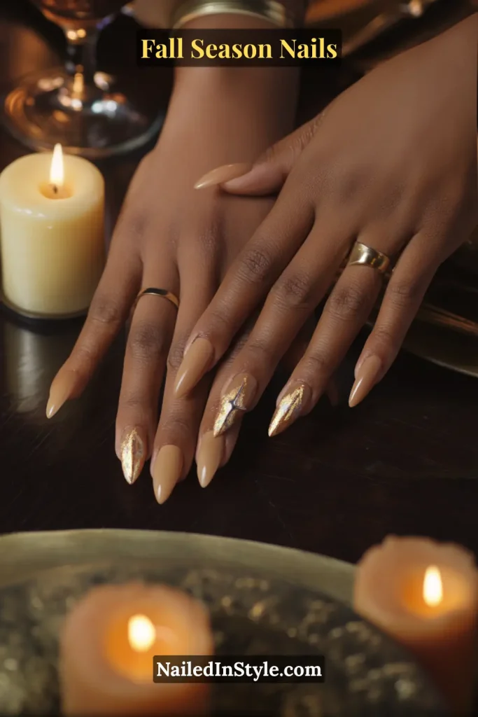 Nude nails with bronze foil starburst accents, styled at a candlelit table.