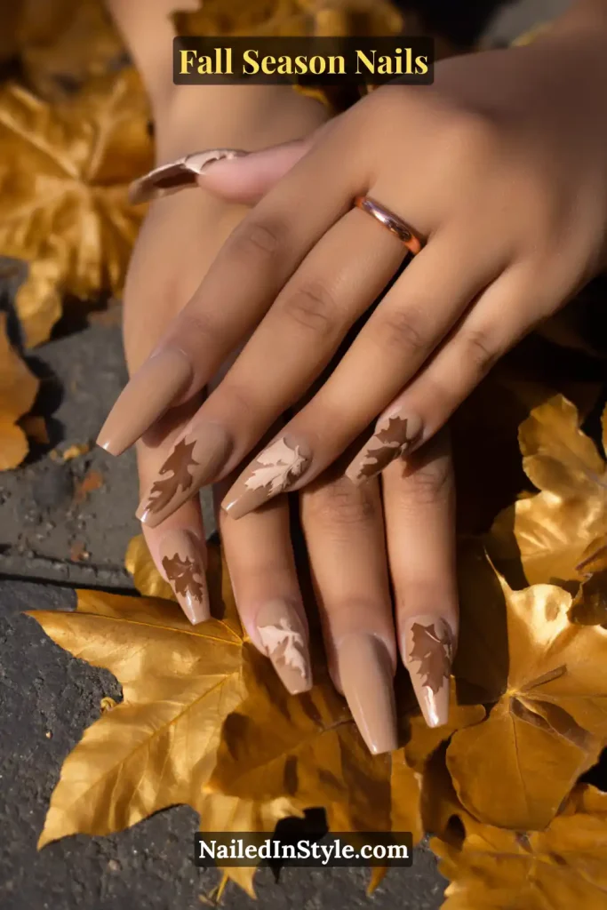Nude nails with maple leaf negative-space accents, styled over autumn leaves on a sidewalk.