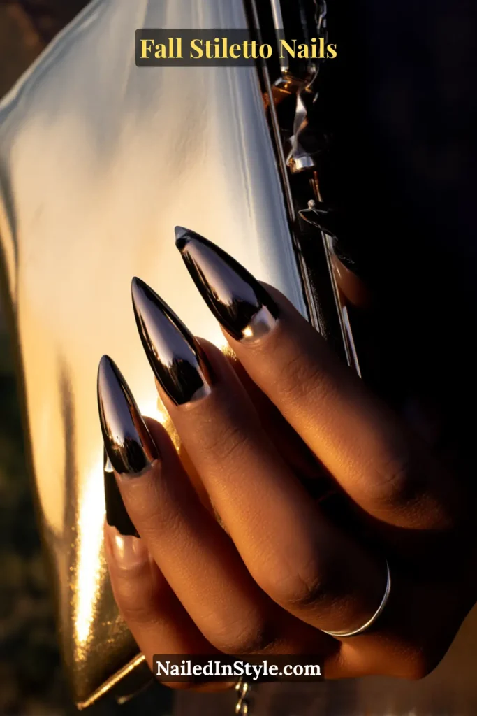 Glossy black stiletto nails with molten pewter drip accents, styled against a metallic clutch clasp.