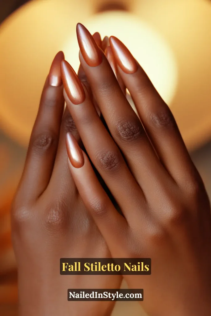 Bronzed stiletto nails glowing with ember aura effect, styled with hands near a warm golden lamp.