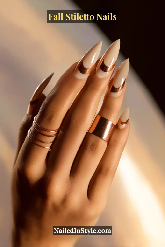 Neutral stiletto nails with negative-space copper crescents near the cuticle, styled with jewelry in warm light.