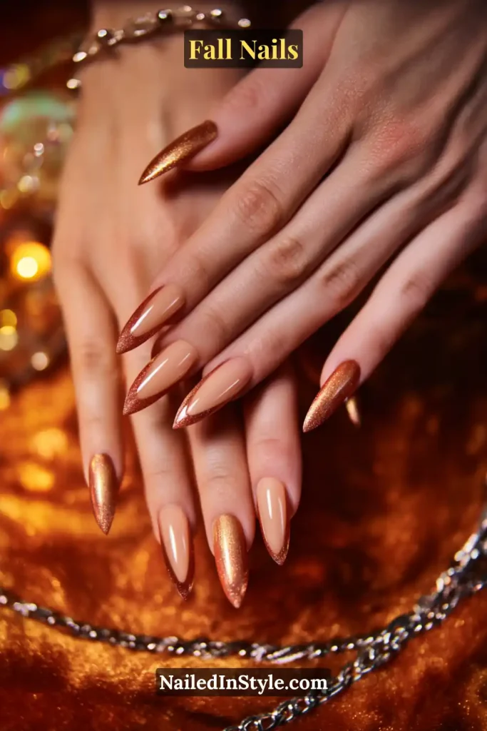 Stiletto fall nails in Copper Halo Coquette design with beige center and soft copper glow edges, styled with jewelry in warm light.