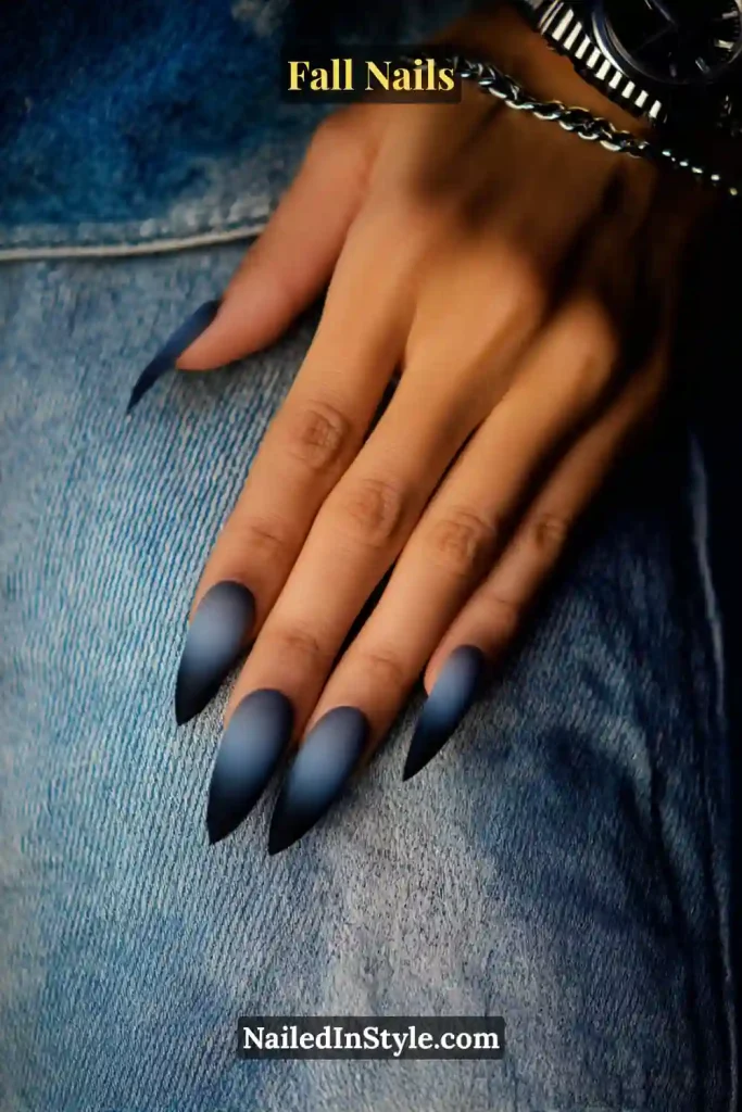 Stiletto fall nails in Denim Smoke Ombré with navy fading to charcoal, styled against denim jeans and a silver watch.