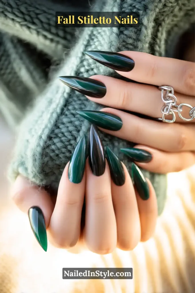 Glossy forest green stiletto nails with flame-inspired tips, styled against a chunky knit scarf.