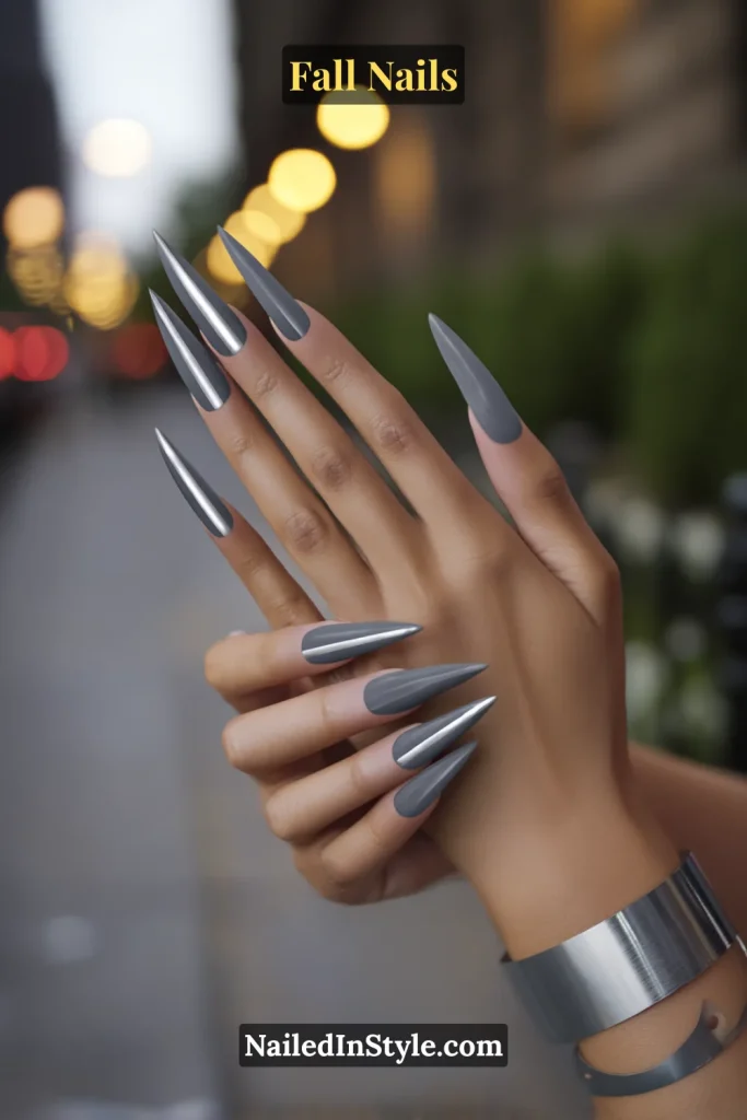 Stiletto fall nails in Graphite Strobe with a gunmetal base and razor-thin silver center line, styled on a city sidewalk at dusk.