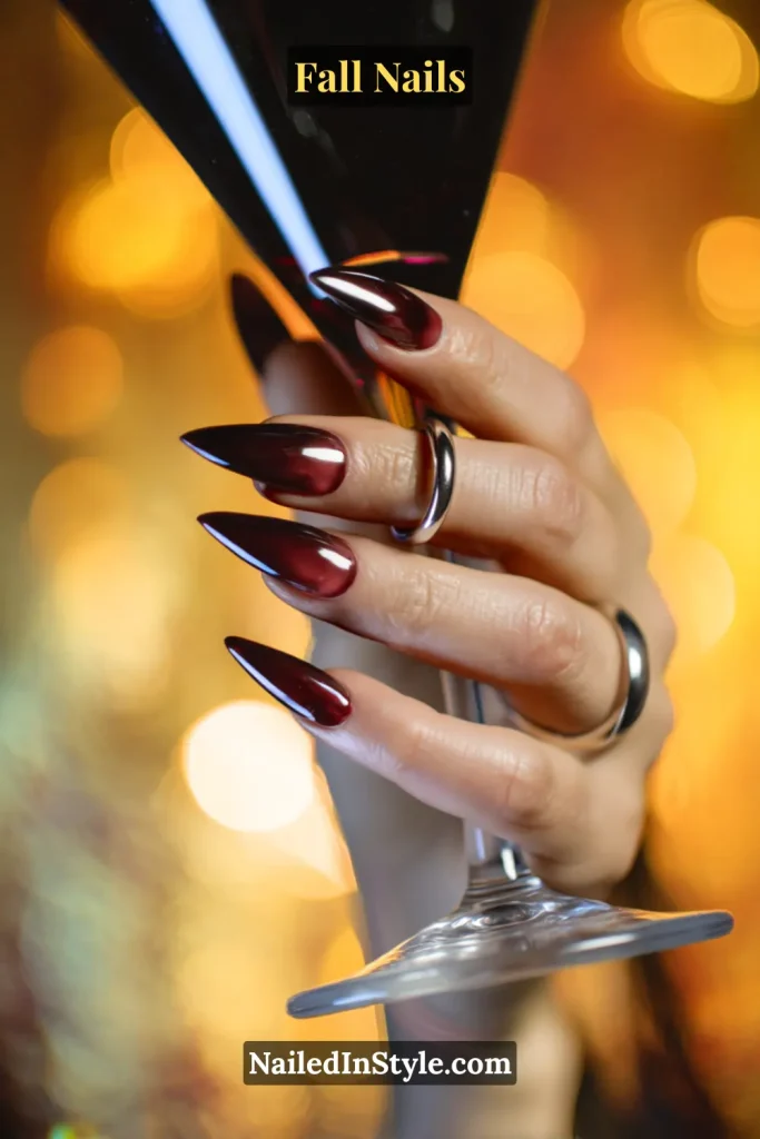 Stiletto fall nails in Moody Merlot Aura with deep merlot center fading to smoky edges, styled holding a stemmed glass.