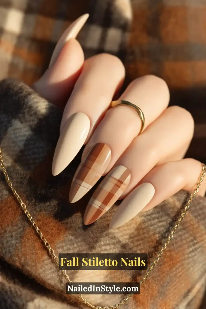 Stiletto nails in glossy nude with diagonal plaid slashes on two accent nails, styled over a tweed coat.