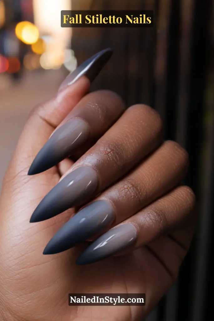 Slate ombre stiletto nails blending from dove grey to charcoal, shot outdoors at dusk.