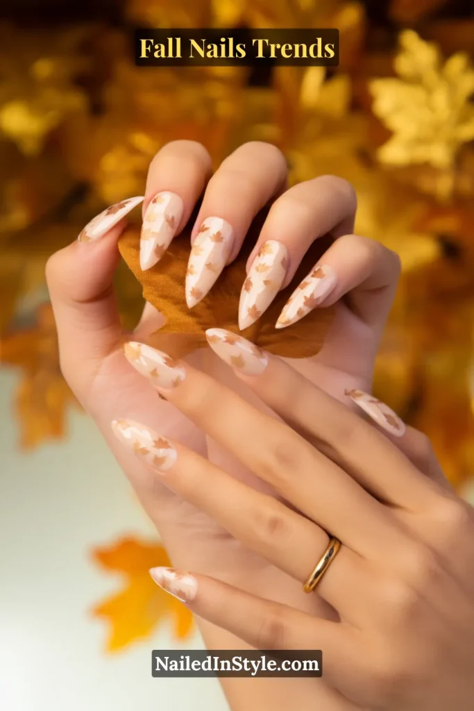 Fall maple leaf accent nails with a nude base decorated with tiny leaf decals, styled while holding autumn leaves against a golden seasonal backdrop.