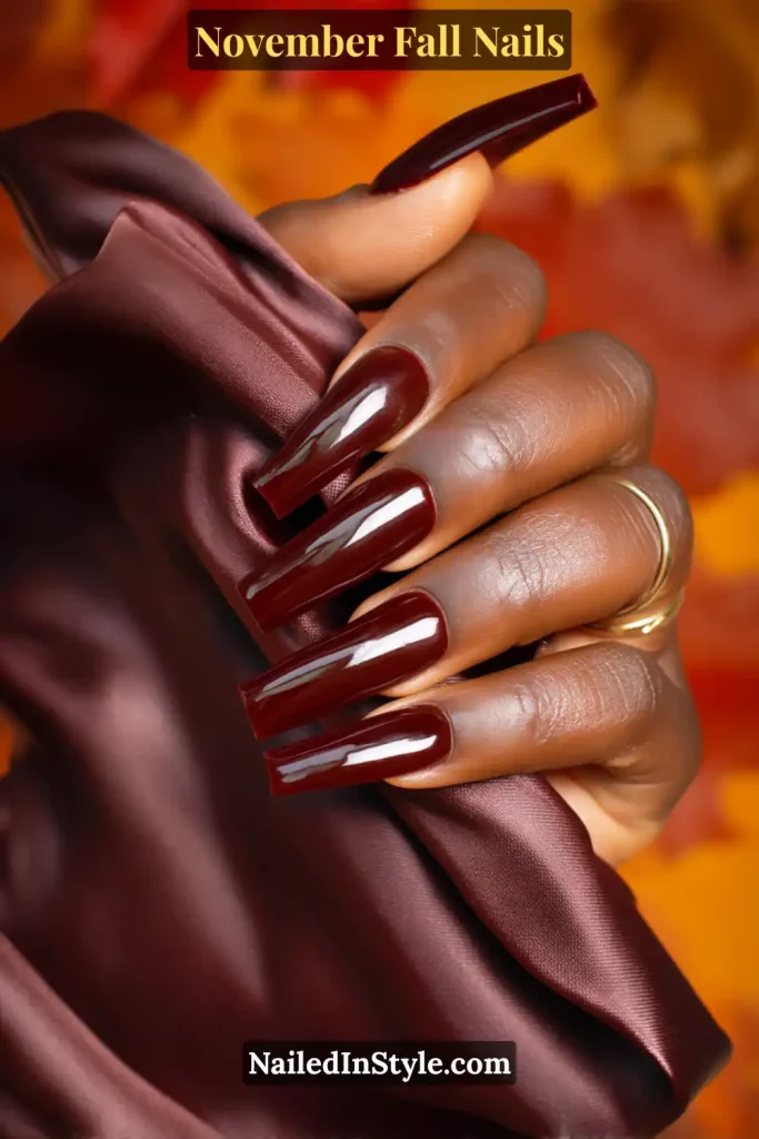 November fall nails in an almost-black cherry shade with a high-gloss glass finish, styled while holding a satin clutch.