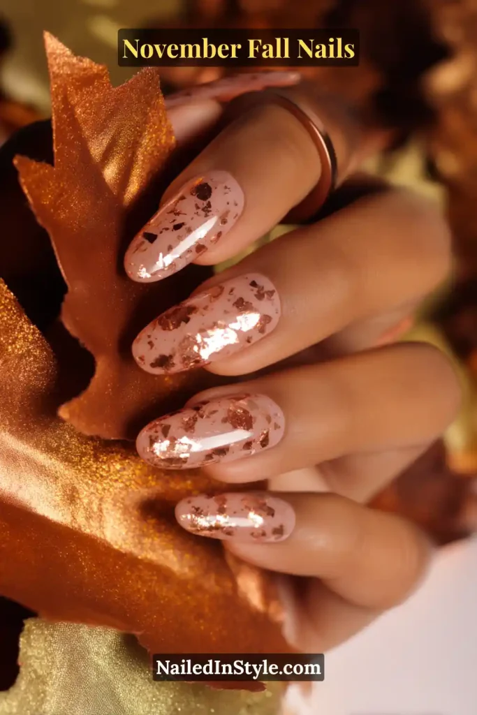 November fall nails in a neutral base with scattered bronze foil, styled to resemble autumn leaves against a cozy fall backdrop.
