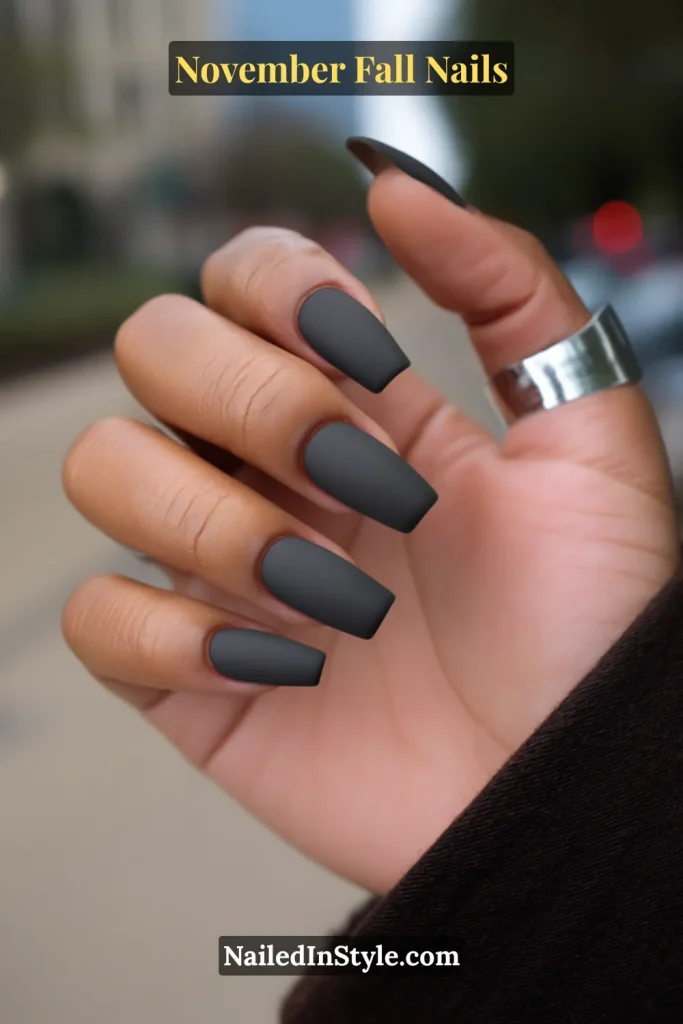 November fall nails in matte charcoal on short square tips, styled against a city sidewalk with a trench coat.
