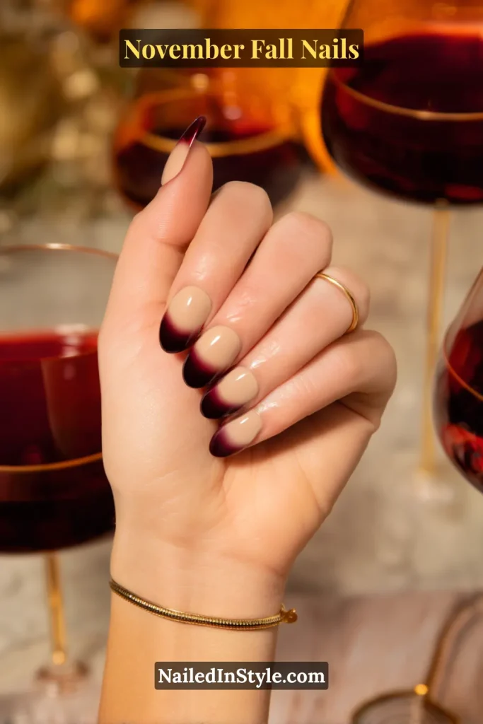 November fall nails in a nude-to-fig wine ombre fade, styled with soft almond tips against a wine glass backdrop.