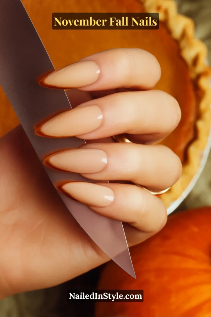 November fall nails in warm nude with thin maple French tips, styled while holding a pumpkin pie server.