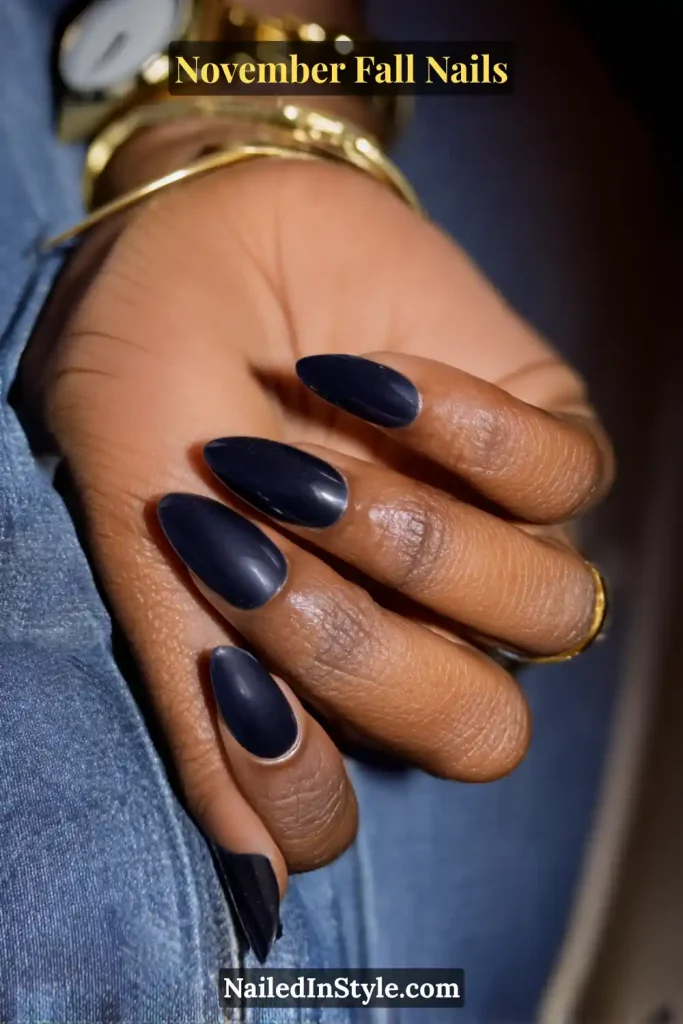 November fall nails in glossy inky navy, appearing black indoors and deep blue in daylight, styled with a denim cuff and gold watch.