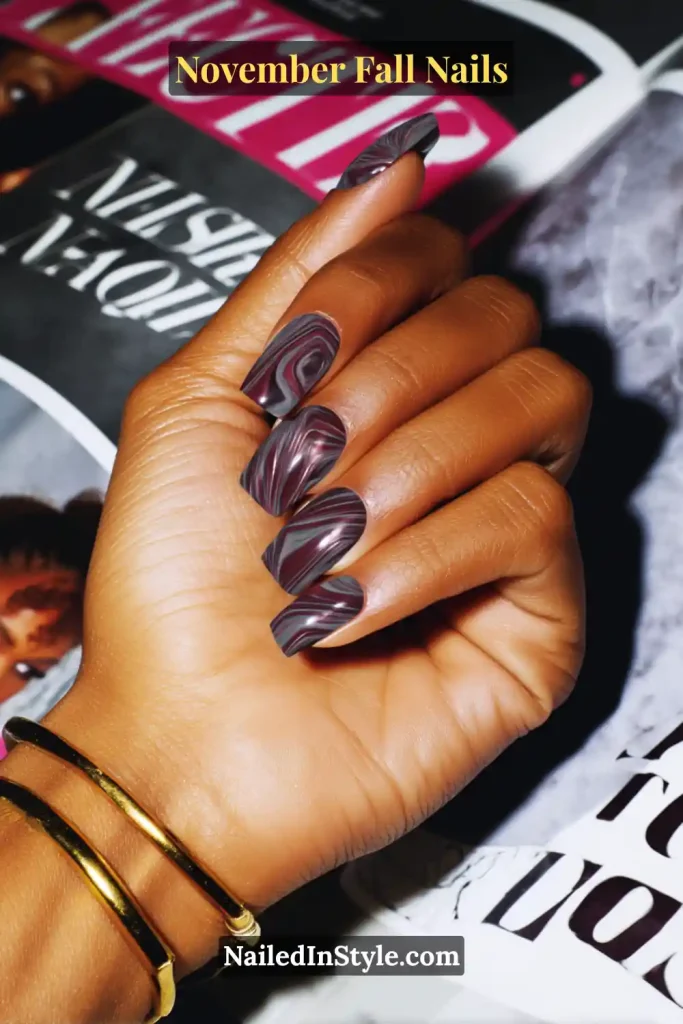 November fall nails with plum and smoky marble swirls, styled on long square nails over an open fashion magazine.