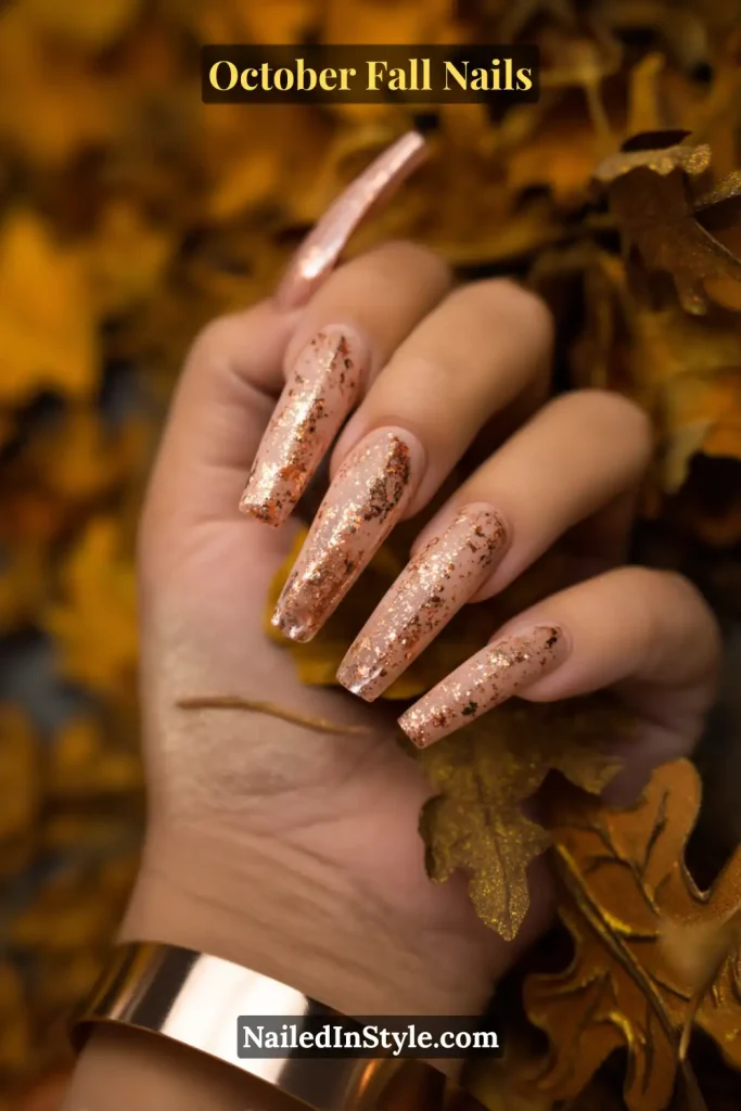 October fall nails with a neutral base dusted in bronze flecks, long coffin shape, styled over fallen autumn leaves.