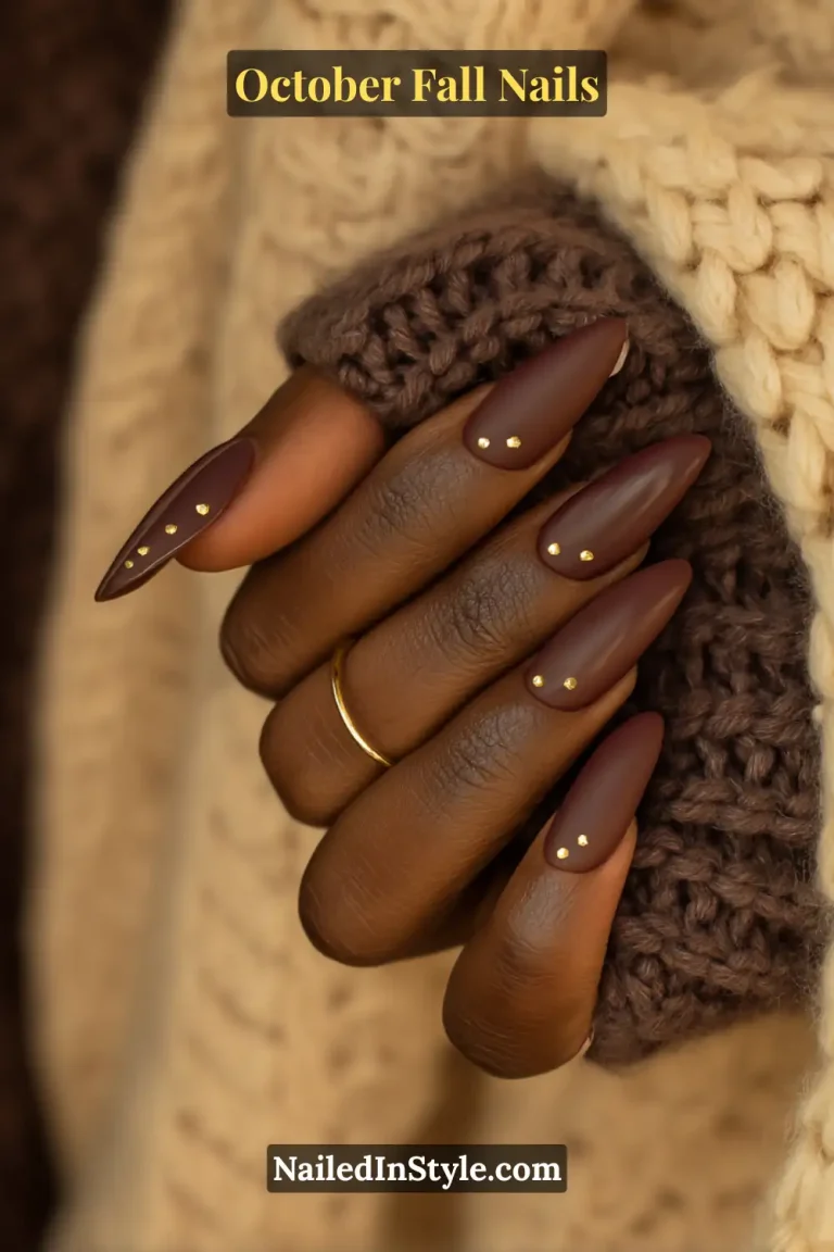 October fall nails in a matte cocoa crème with tiny gold dots at the cuticle, almond shape, styled against chunky knit sleeves.