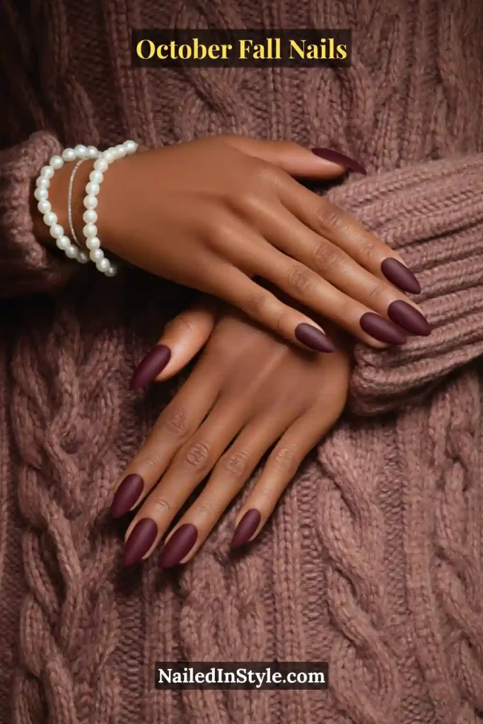 October fall nails in matte mulberry polish on almond nails, styled against a cozy cable-knit sweater; plush, autumn-ready finish.