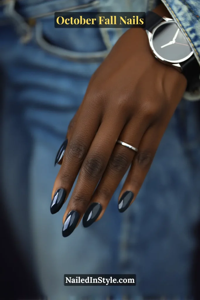 October fall nails in inky navy polish with a glossy finish, almond shape, appearing black indoors and blue in daylight, styled with a denim cuff and watch.
