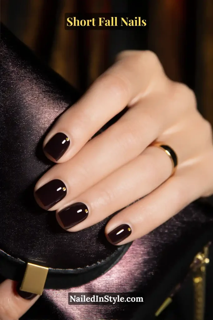 Short black cherry nails with a micro-gold dot near the cuticle, paired with a satin clutch.