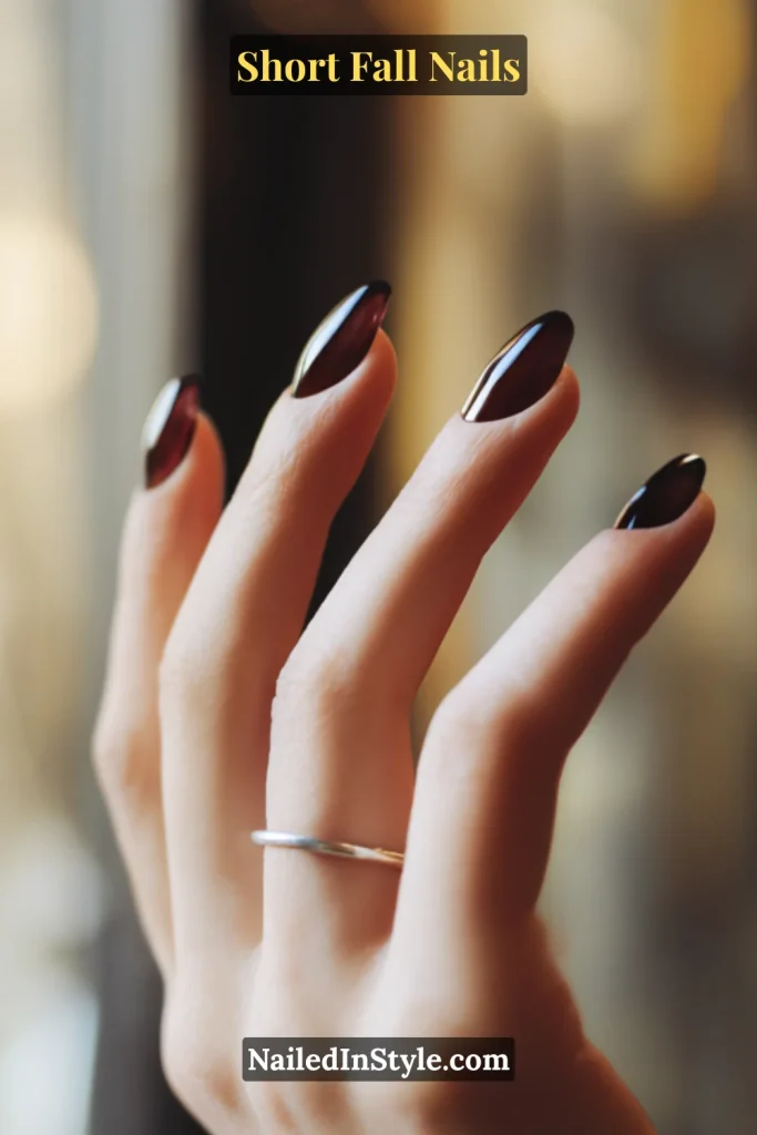 Short almond nails with translucent blackberry jelly polish glowing in warm café window light.