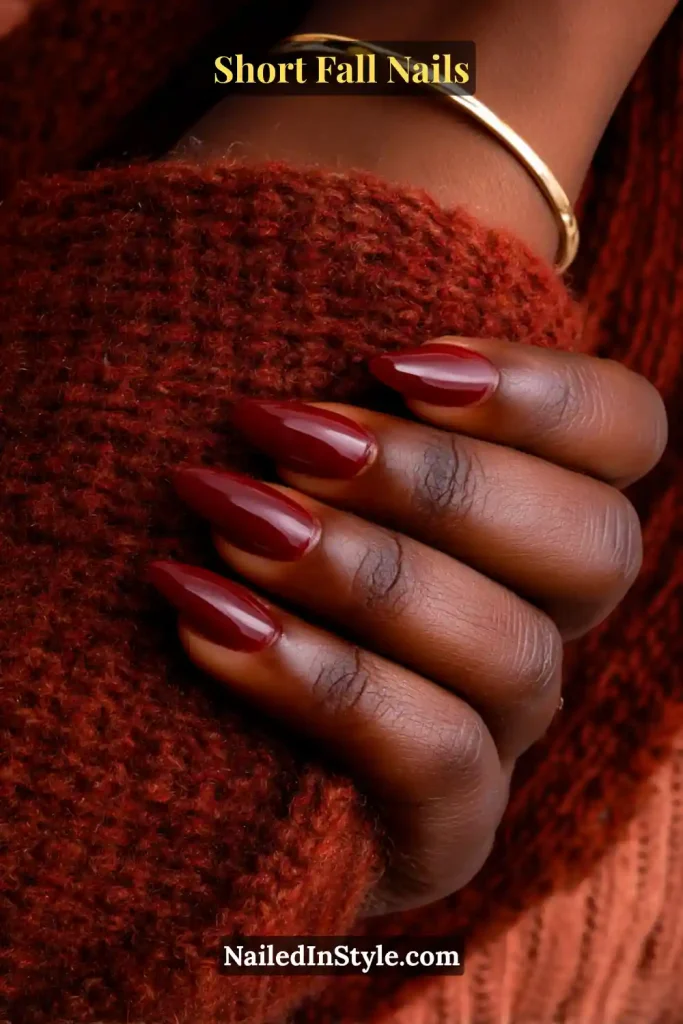 Short almond nails in creamy cranberry red, styled against a cozy cashmere cuff for a chic fall look.