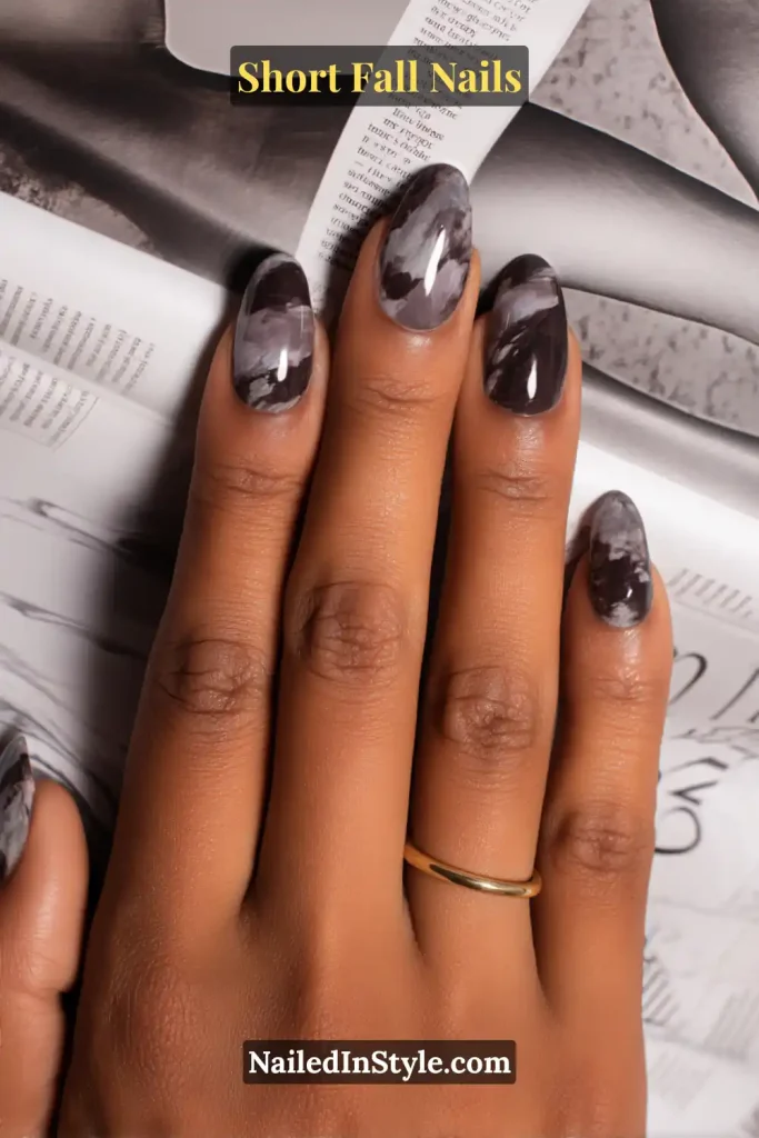 Short almond nails with plum and smoky marble swirls, styled over an open fashion magazine.