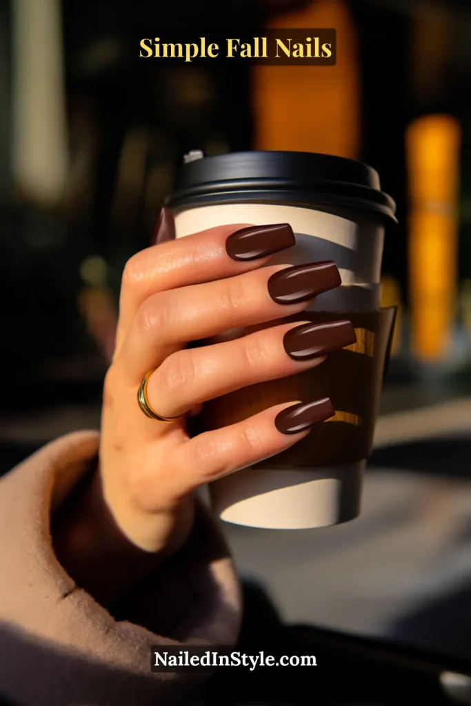 Simple fall nails in deep espresso brown polish, short square shape, holding a coffee cup sleeve; glossy finish with cozy fall vibe.