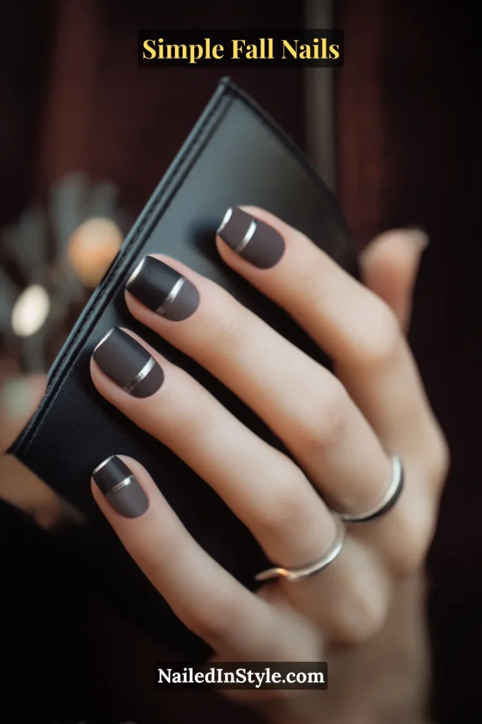 Simple fall nails in a matte charcoal base with a single metallic pinstripe line across each nail, styled while holding a sleek black cardholder.