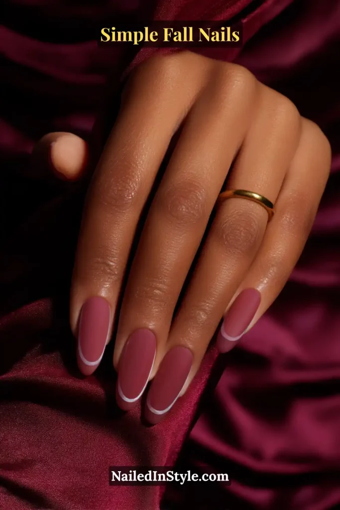 Simple fall nails in sheer plum polish with a thin glossy contour outline around each nail, styled against a deep silk blouse cuff.