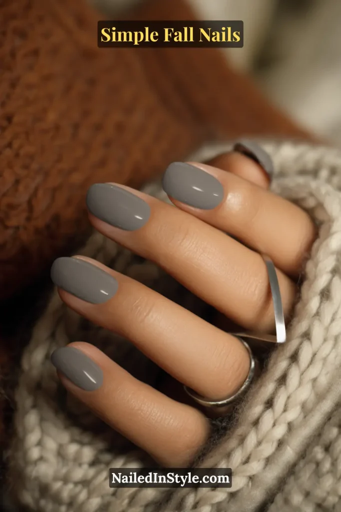 Simple fall nails in a mid-grey crème polish on short squoval nails, styled against a cozy wool throw; chic minimalist fall manicure.