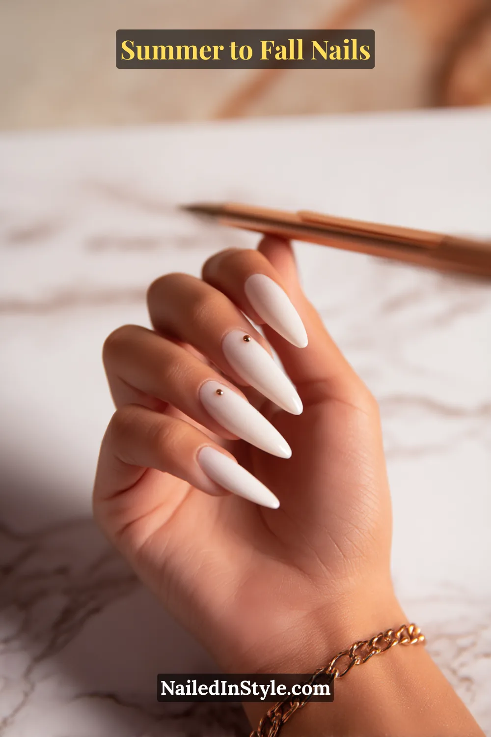 Summer-to-fall stiletto nails in milky white with copper micro-stud accents, rose-gold pen and bracelet, office-ready.