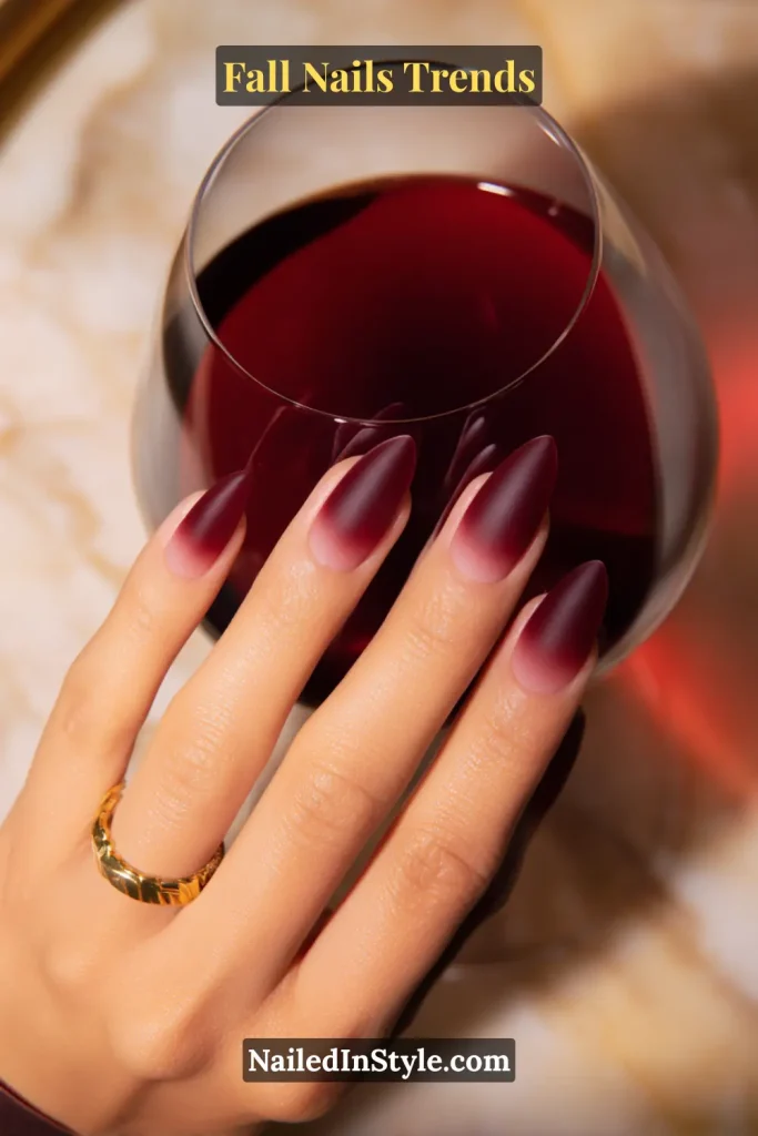 Fall wine ombré nails blending nude into deep red, styled while holding a glass of red wine for a chic seasonal statement.