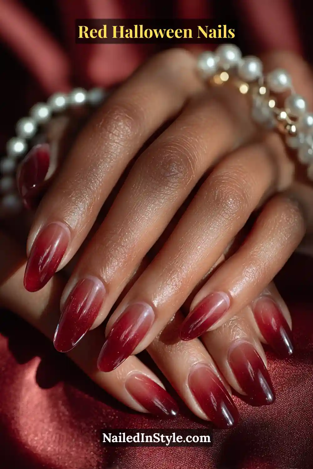 Long almond nails in translucent wine-red jelly with glowing ember tint near the tips; radiant under warm evening light; paired with a pearl-and-gold bracelet; complements medium to deep skin tones with syrupy depth and elegance.