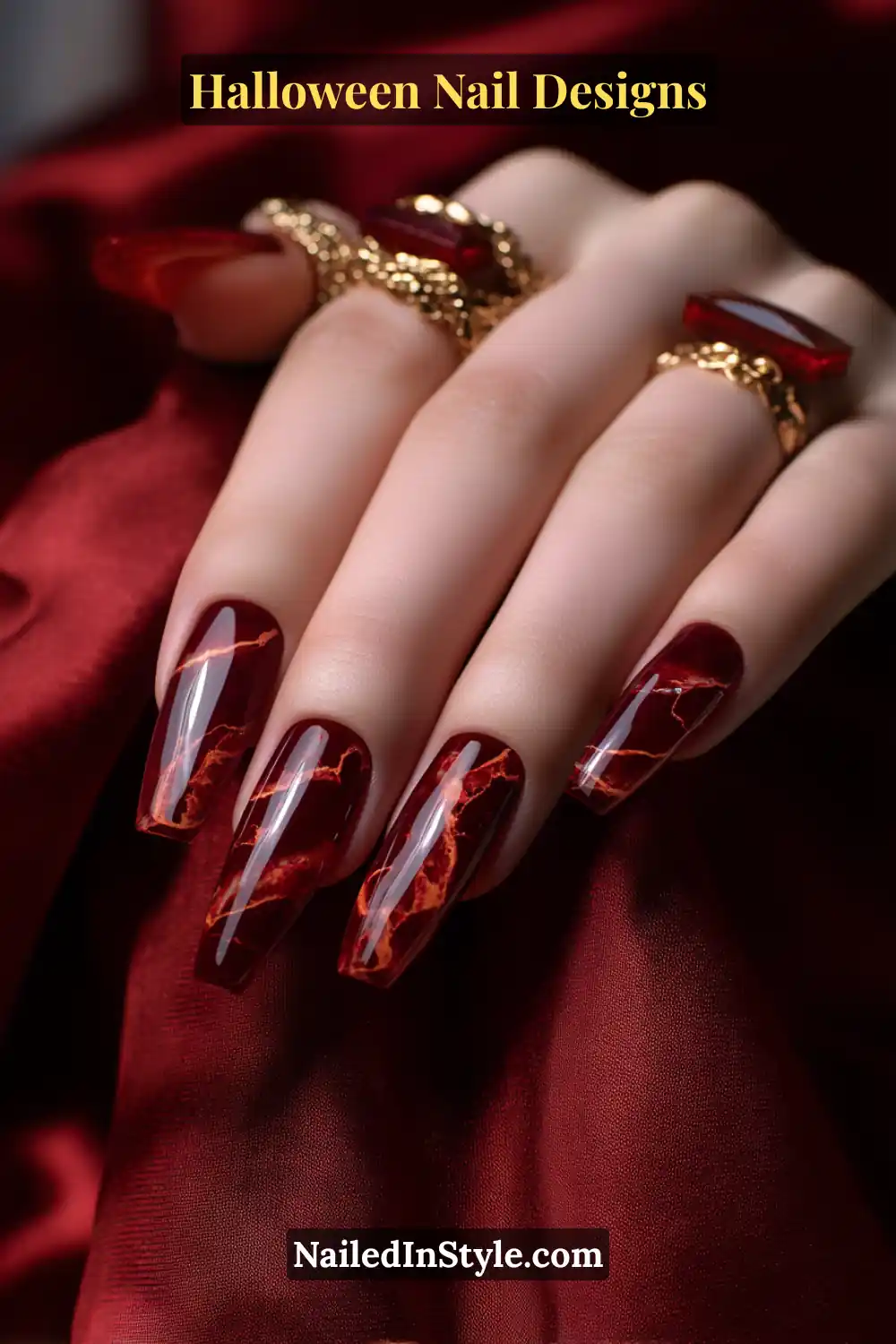 Close-up of long coffin nails featuring a rust-to-crimson marble rim design with a clear glossy center, styled with gold gemstone rings and red satin fabric for a rich Halloween aesthetic.