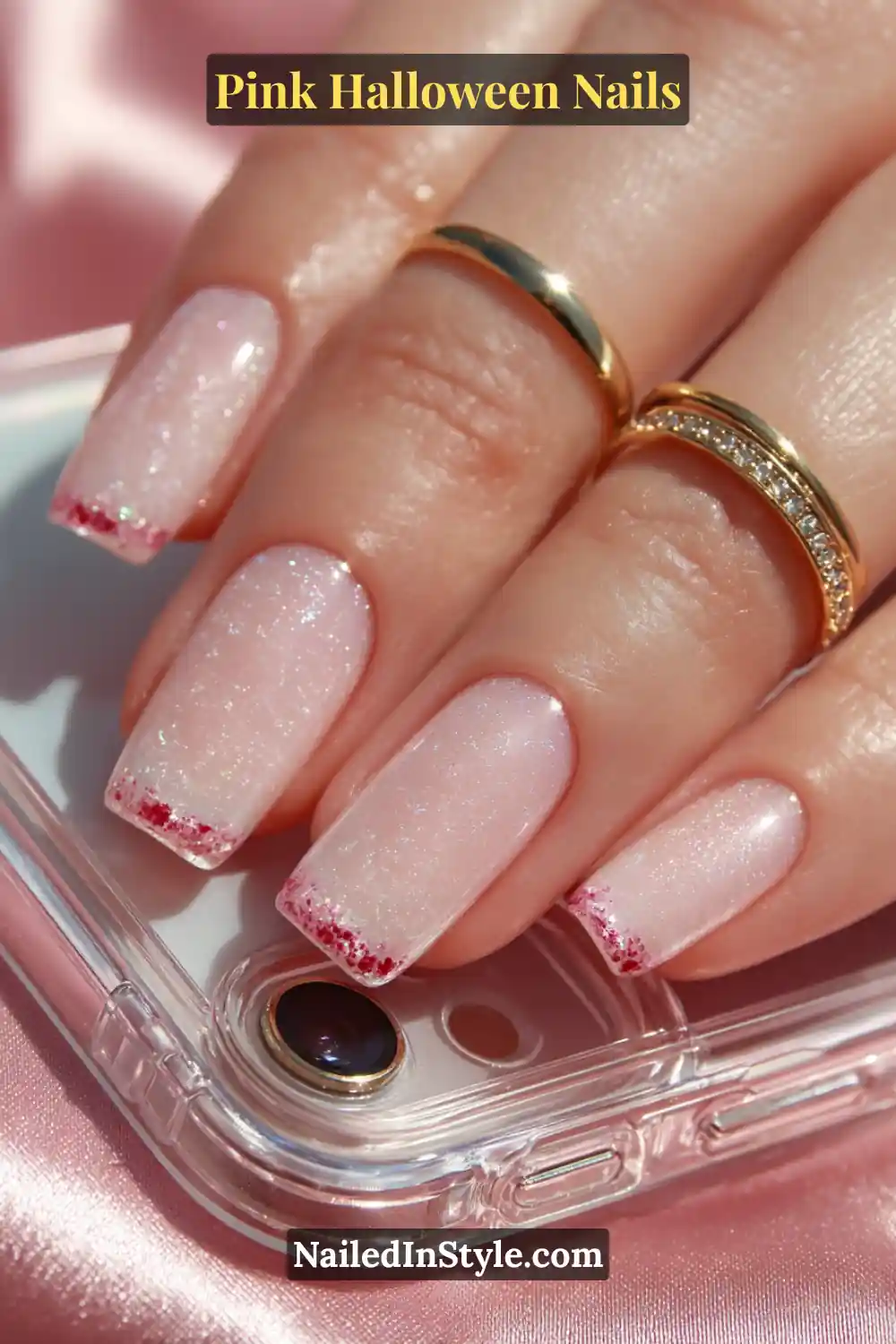 Pink Halloween nails featuring a pastel pink base with glossy red 3D drip domes on short square nails, styled with gold rings and a mirrored phone case.